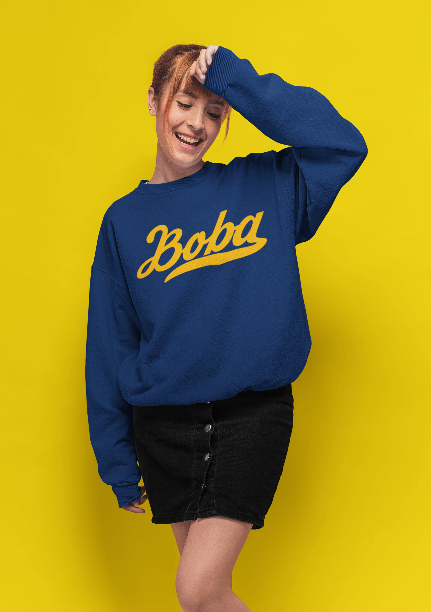 Woman wearing a UC Boba shirt smiling against a yellow background